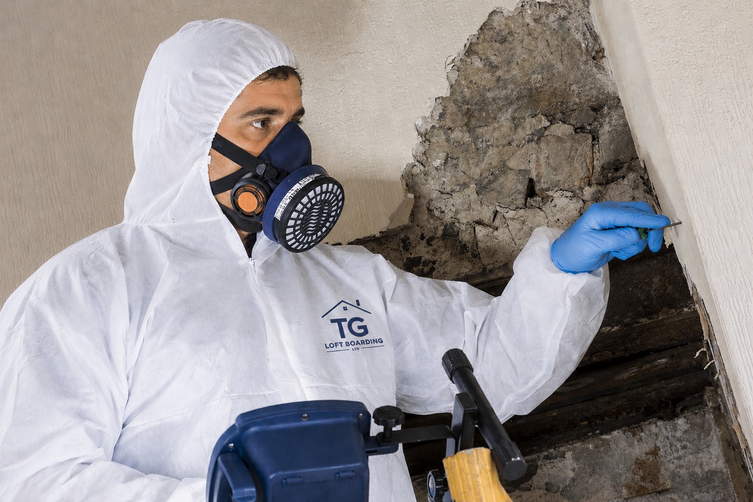 TG Loft Boarding technician in a protective suit and respirator removing asbestos from a loft